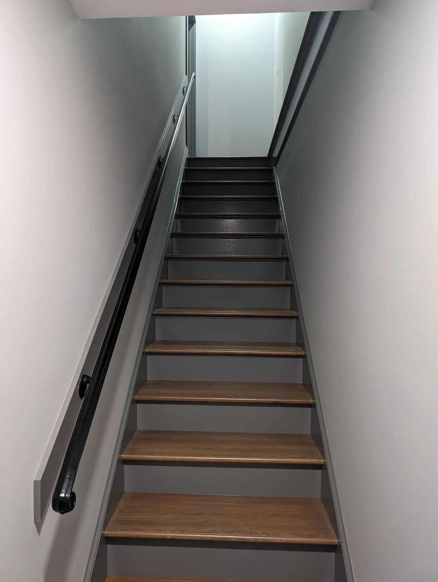 Custom basement stairs with stained oak treads, painted risers, and black handrail